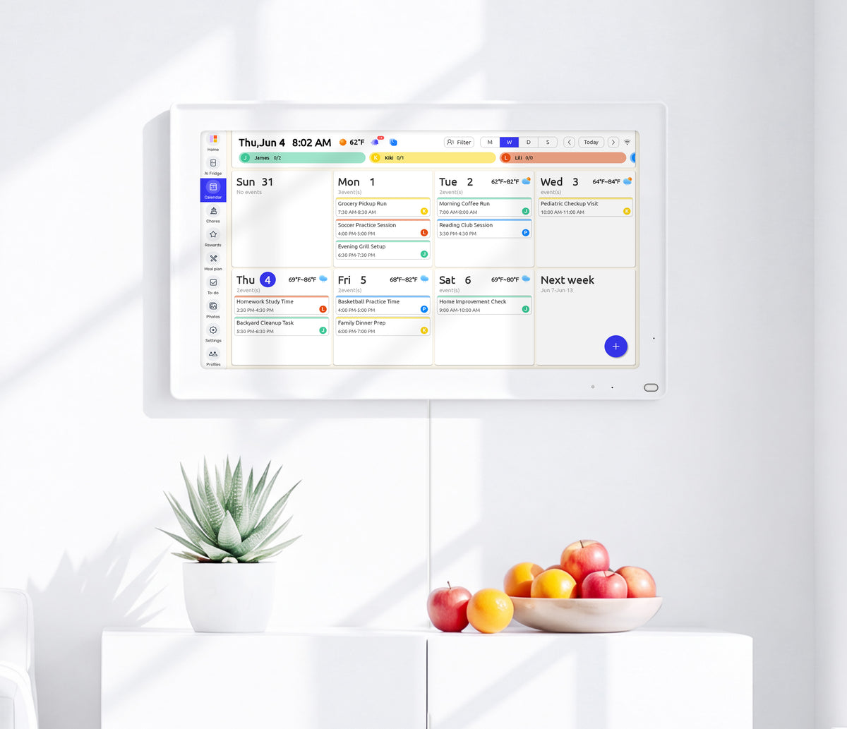white everblog magnetic tablet mounted on wall showing family calendar schedule, home kitchen scene with fruit and succulent plant